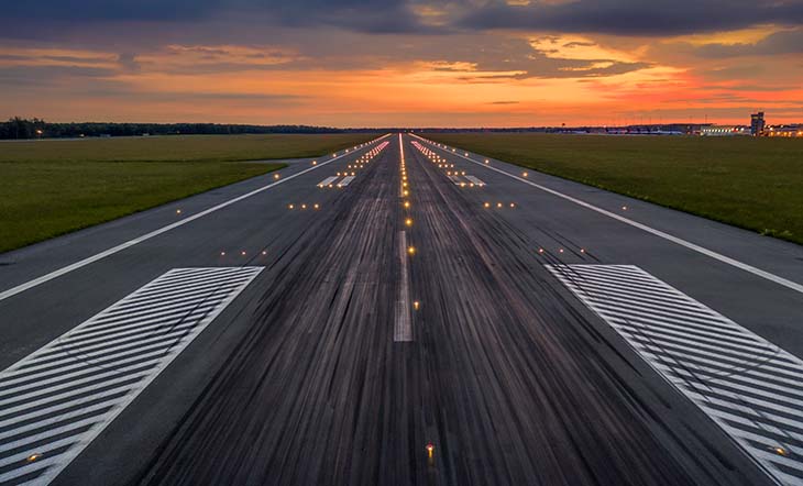 Used concrete asphalt airport empty runway with many braking marks, markings for landings and all navigation lights on