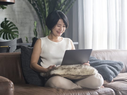 woman sitting on the couch using a laptop while smiling